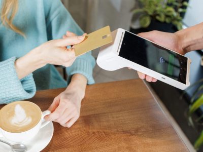 Customer pays for coffee using NFC bank card on handheld POS terminal during tableside checkout in cafe contactless payment technology